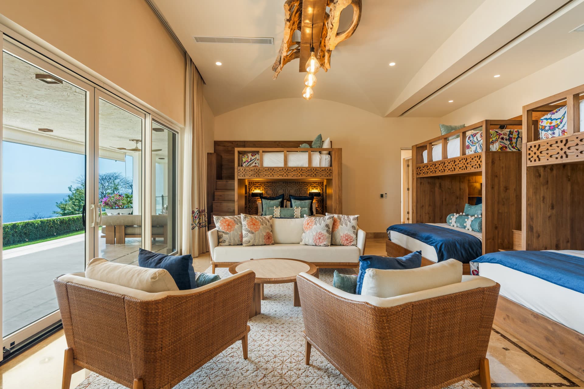Bunk room at Villa Luciérnaga — three bunk units sleeping nine children, driftwood chandelier, and direct Pacific views through floor-to-ceiling glass