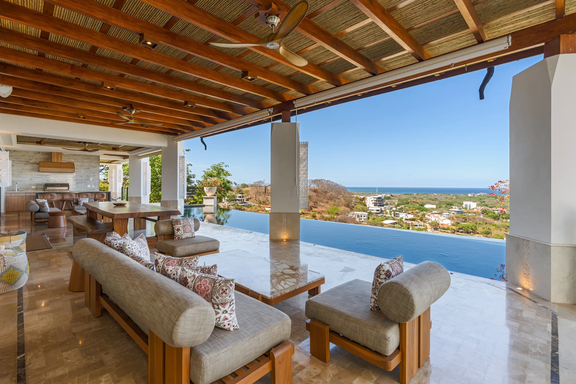 Covered terrace lounge at Villa Luciérnaga beside the infinity pool edge, Tamarindo and the Pacific beyond